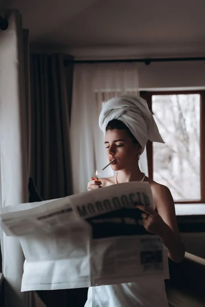 Piękna młoda kobieta w ręczniku pali papierosa i czyta gazety — Zdjęcie stockowe