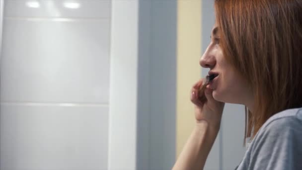 Mooie jonge vrouw in de badkamer borstelen haar tanden — Stockvideo
