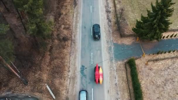 Несколько вагонов с байдарками на багажнике на крыше едут по дороге среди деревьев — стоковое видео