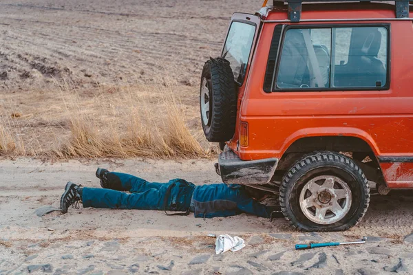 Чоловік лежить під машиною 4x4 на брудній дорозі — стокове фото