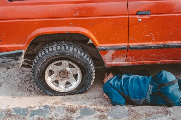 Чоловік лежить під машиною 4x4 на брудній дорозі — стокове фото