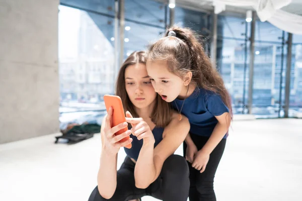 체육관에서 비디오를 보기 위해 핸드폰을 사용하는 어머니와 소녀 — 스톡 사진