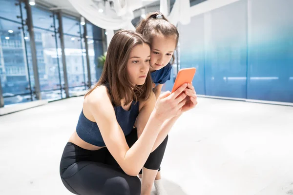 Mor og jente som bruker telefon i gymsalen for å se på video – stockfoto