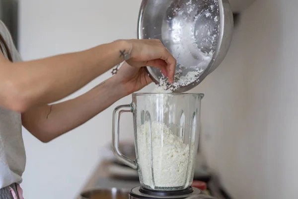 Woman pouring cottage cheese into a blender in the kitchen