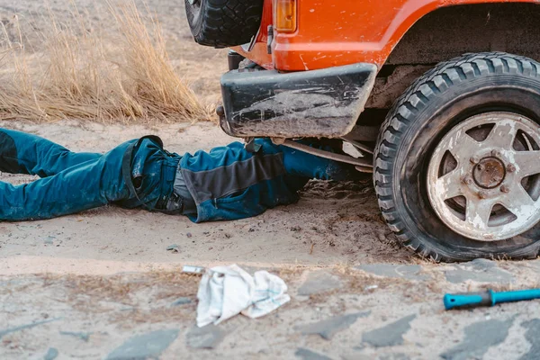 Homem encontra-se sob um carro 4x4 em uma estrada de terra — Fotografia de Stock