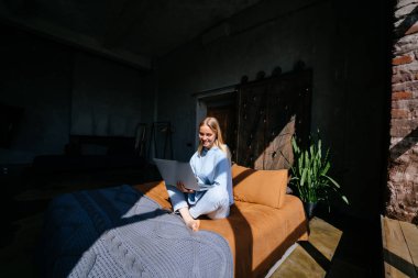 Gülümseyen çekici kadın yatakta laptop kullanarak yatıyor