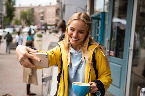 Encantadora jovem loira com smartphone tirar selfie na rua — Fotografia de Stock