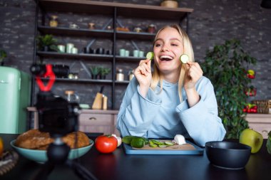 Genç ve güzel sarışın mutfakta yemek pişirirken videolar çekiyor.