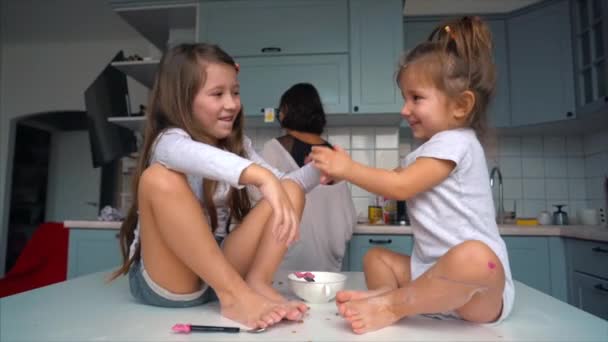 Dwie małe dziewczynki w kuchni siedzą na stole.. — Wideo stockowe