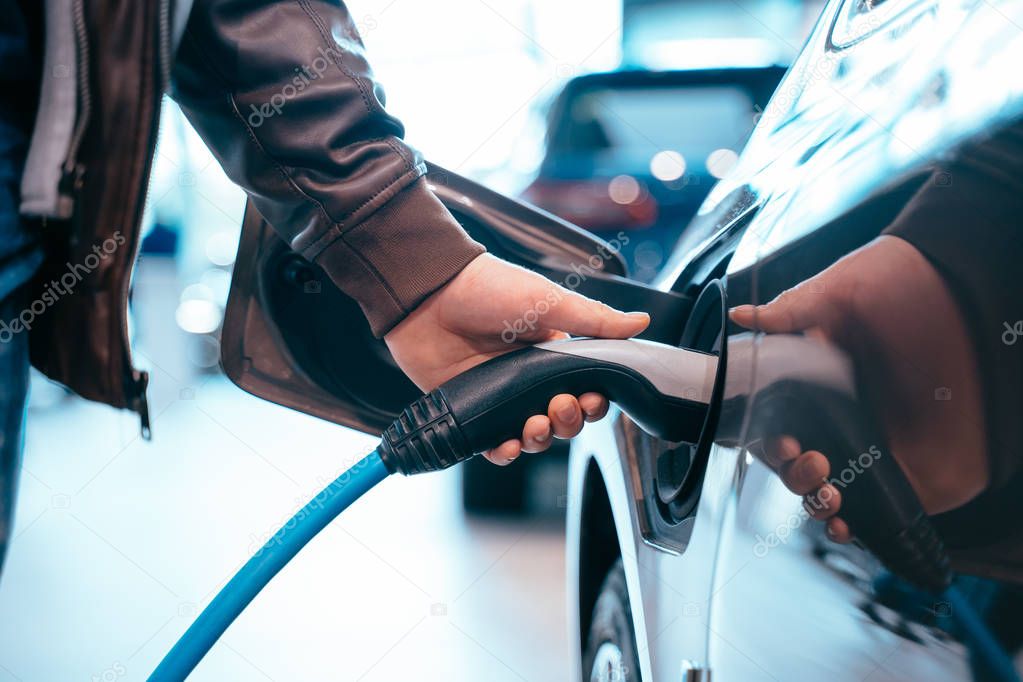 Human hand is holding Electric Car Charging connect to Electric car