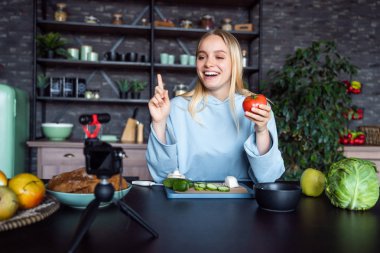 Genç ve güzel sarışın mutfakta yemek pişirirken videolar çekiyor.