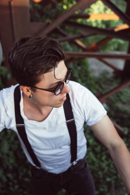 Eski metal yapılar arasında pantolon askısı olan bir adam.