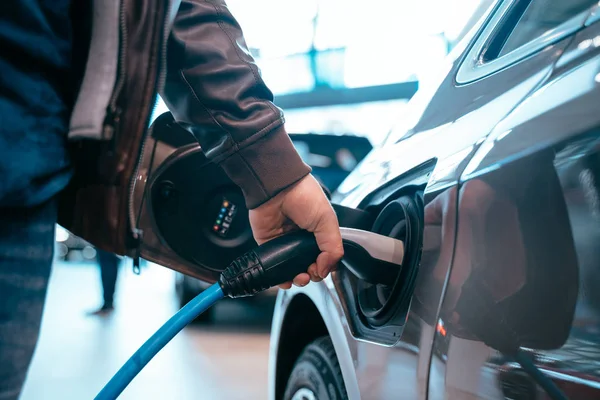 Main humaine tient voiture électrique connexion de charge à la voiture électrique — Photo