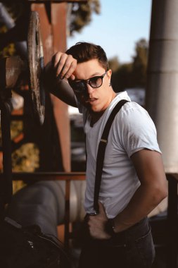 Pantolon askılı bir adam eski borulara ve vanalara poz veriyor.