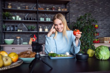 Genç ve güzel sarışın mutfakta yemek pişirirken videolar çekiyor.