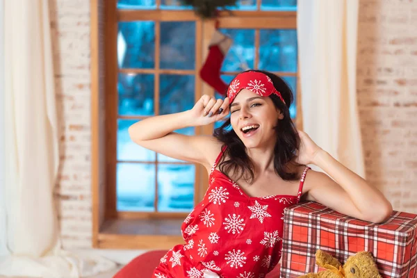 Beautiful woman in pajamas with gift box, window in the background.