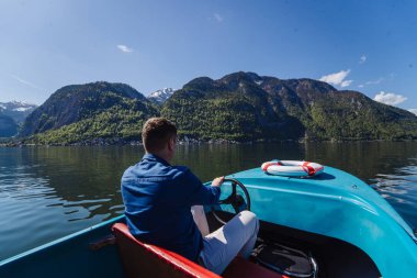 Yakışıklı genç adam bir dağ gölünde motorlu tekne kontrol ediyor.