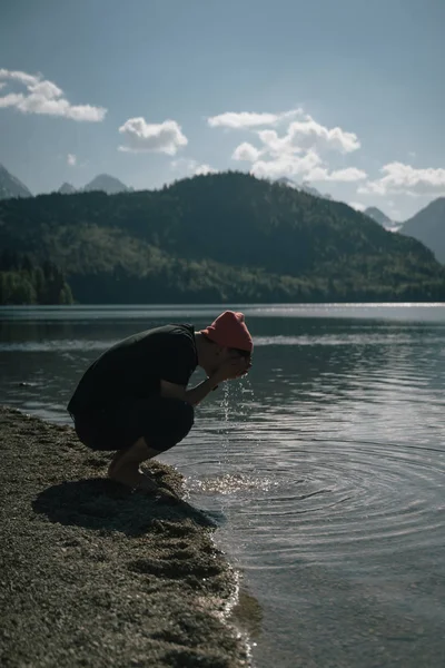 En man tvättar händerna på stranden av en skog sjö — Stockfoto