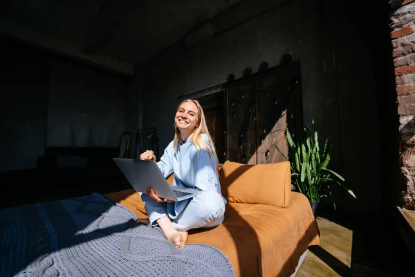 Gülümseyen çekici kadın yatakta laptop kullanarak yatıyor