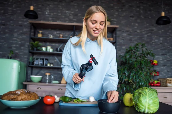 Genç ve güzel sarışın mutfakta yemek pişirirken videolar çekiyor.