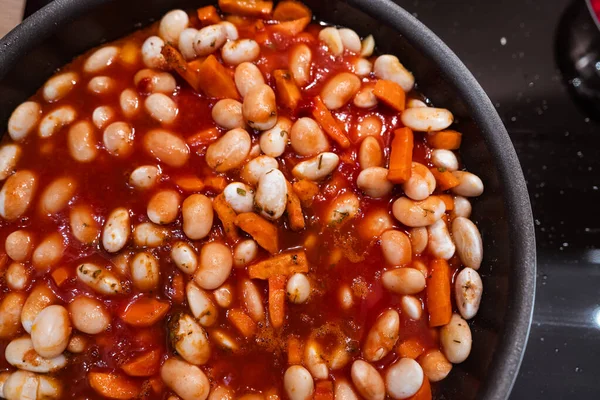 Morötter, vitlök och bönor med tomatsås i en kastrull före matlagning. Stäng slöja — Stockfoto