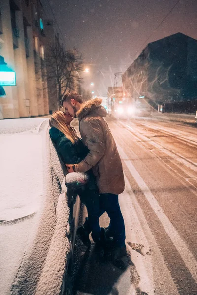 Jovem casal adulto beijando uns aos outros na neve coberta de rua — Fotografia de Stock