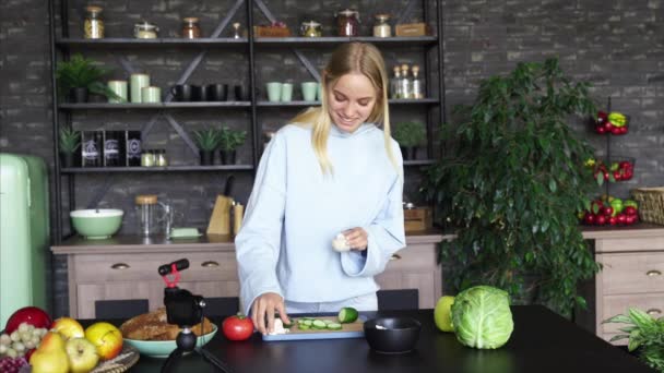 Joven hermosa rubia toma videos como ella cocina en la cocina — Vídeos de Stock