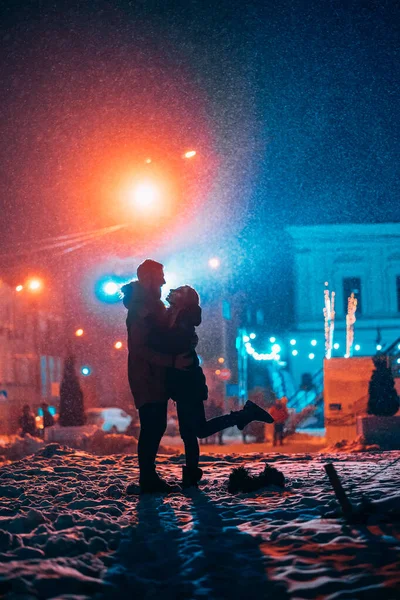Jovem casal adulto em cada outros braços na neve coberta de rua . — Fotografia de Stock