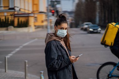 Açık havada akıllı telefon kullanan koruyucu maskeli bir kız. COVID 19. Dünya koronavirüs salgını.
