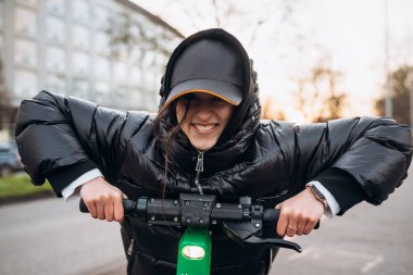 Sonbahar şehrinde elektrikli scooter kullanan ceketli bir kadın..