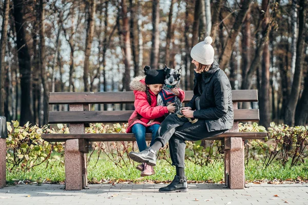 Felice madre e sua figlia con il cane appoggiato su una panchina — Foto Stock