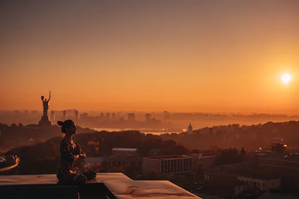 Γυναίκα κάνει γιόγκα στη στέγη ενός ουρανοξύστη στην μεγάλη πόλη. — Φωτογραφία Αρχείου