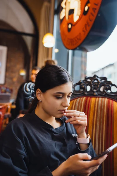 Gadis muda cantik beristirahat di kursi besar yang lembut di kafe, mengobrol di telepon — Stok Foto