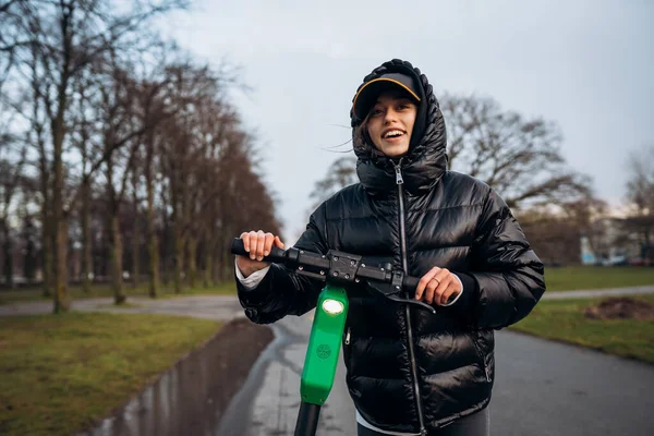 Mulher em uma jaqueta em uma scooter elétrica em um parque de outono. — Fotografia de Stock