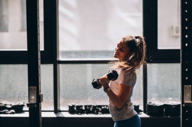 İnce atletik kız halterleriyle fiziksel egzersiz yapıyor..