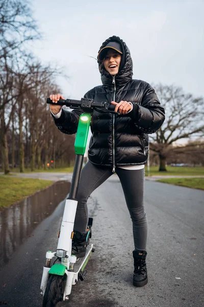 Egy nő zakóban egy elektromos robogón egy őszi parkban.. — Stock Fotó