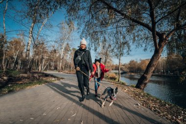 Mutlu anne ve kızı güz parkında köpekle yürüyor.