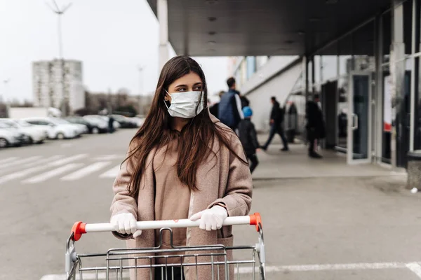 Молодая женщина в защитной маске против коронавируса 2019-nCoV толкает корзину. — стоковое фото