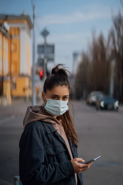 Девушка в защитной маске с помощью смартфона на открытом воздухе. COVID 19. Мировая пандемия коронавируса . — стоковое фото