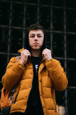 Sarı ceketli genç bir adam şehir caddesinde yürüyor.