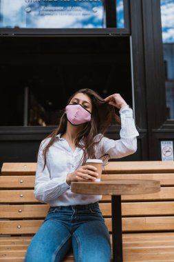Tıbbi maskeli kadın sokakta kahve içiyor.