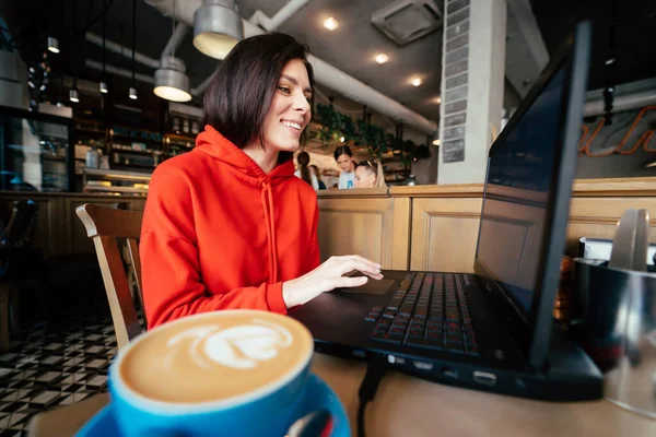 Молодая женщина в баре пьет кофе и пользуется ноутбуком — стоковое фото
