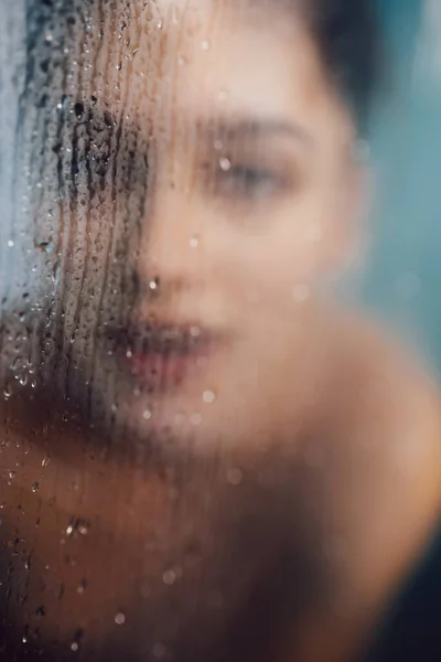Beautiful woman behind the glass with water drops. — Stock Photo, Image