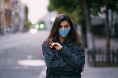 Genç bir kadın, boş sokakta koruyucu tıbbi maske takan biri.