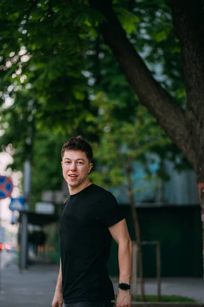 Молодий дорослий чоловік в чорній футболці і джинсах гуляє по міській вулиці — стокове фото