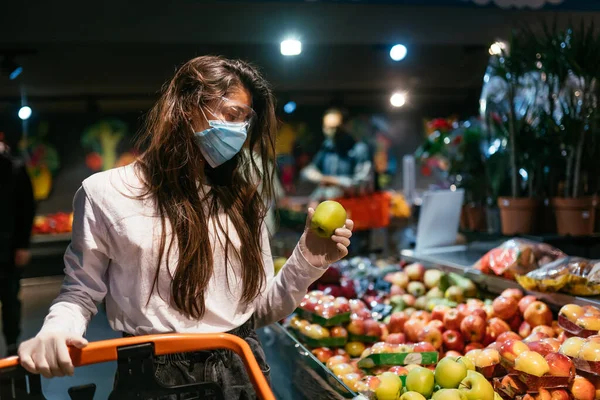 A menina com máscara cirúrgica vai comprar maçãs. — Fotografia de Stock