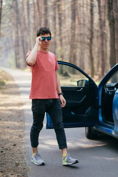 Hombre guapo de pie en la carretera cerca de la puerta abierta de su coche. —  Fotos de Stock