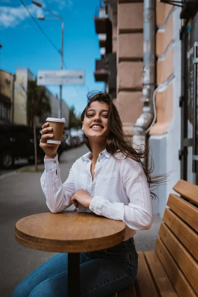 Beautiful young woman in street cafe drinks coffee