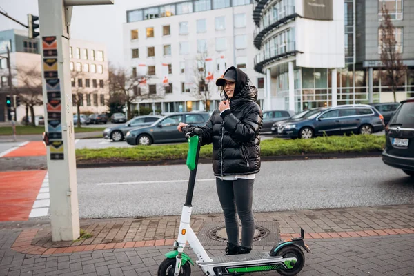 Vrouw in een jasje op een elektrische scooter in een herfststad. — Stockfoto