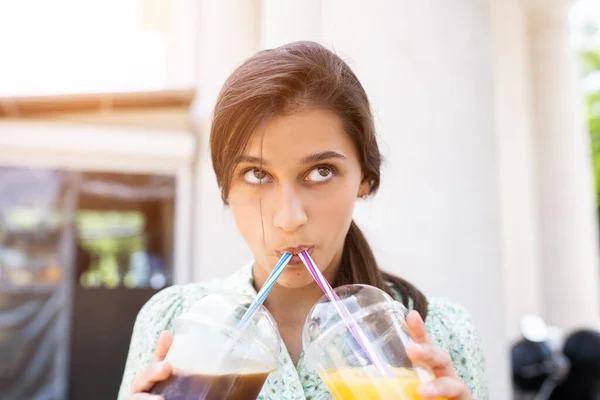 Junge Frau trinkt zwei Cocktails mit Eis in Plastikbechern mit Stroh — Stockfoto